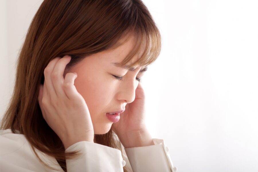 耳元辺りを押さえて不快そうにしている女性
